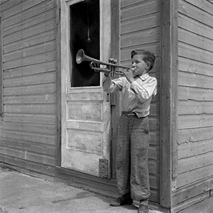 Photographie noir et blanc d’un jeune garçon jouant de la trompette.