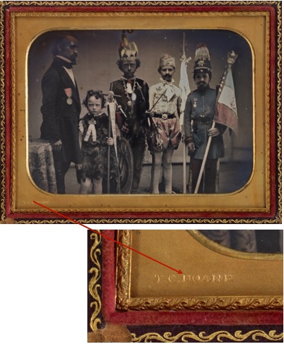 Photographie colorée à la main d'un homme et de quatre garçons costumés. La photographie est dans un boîtier avec un passe-partout de laiton. Le coin inférieur gauche porte une inscription étampée.